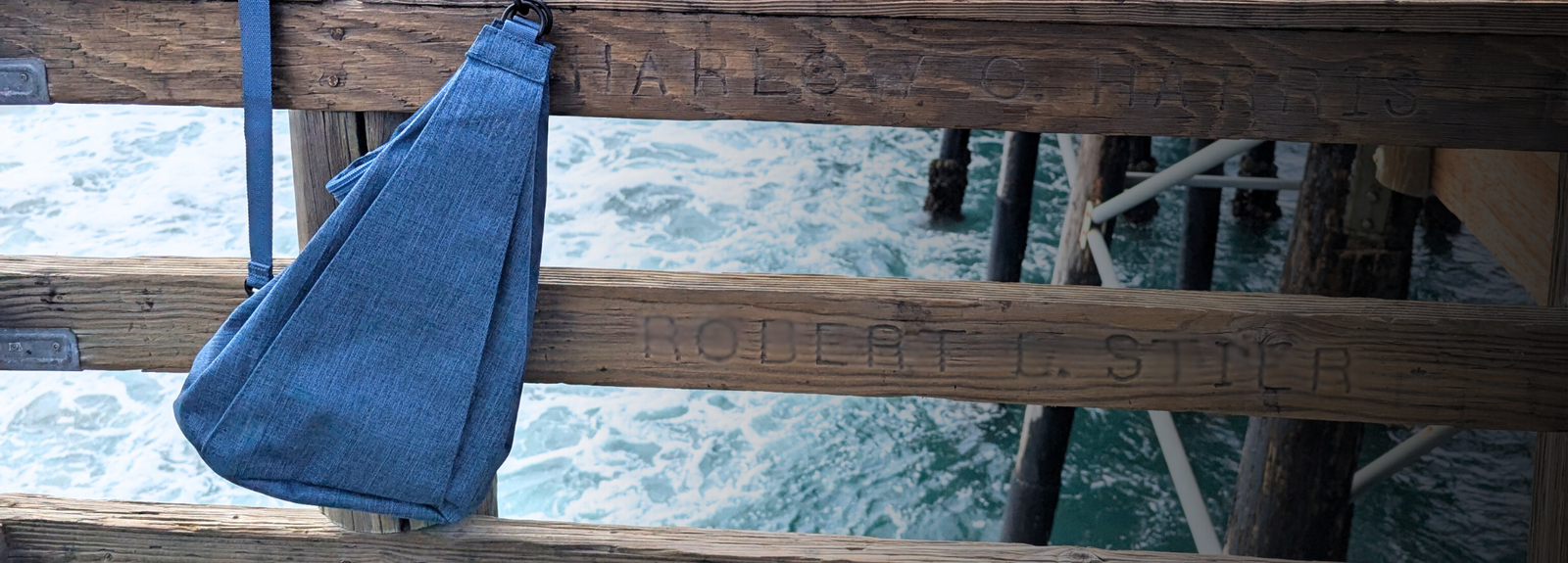 Blue bag hanging on a wooden pier with water in the background