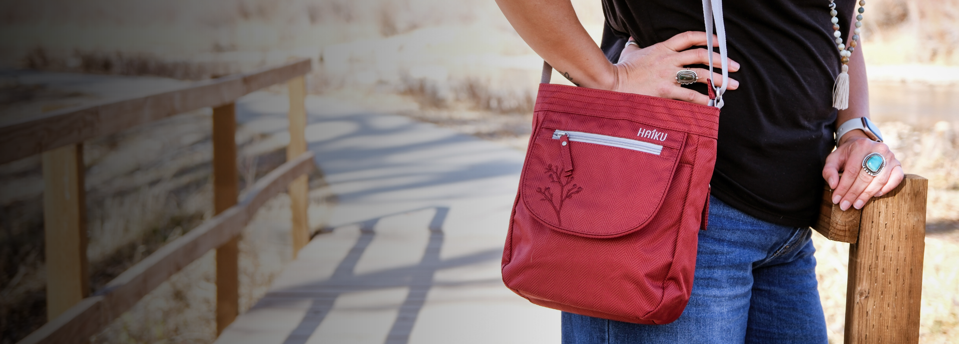 Person holding a red crossbody bag on a wooden bridge.