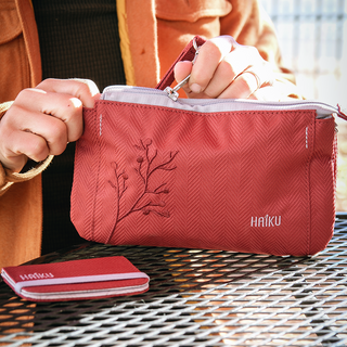 Red pouch with floral design and 'Haiku' branding held by a person outdoors.